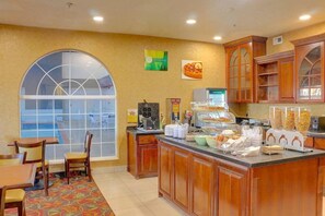 A hotel kitchen with a large window, wooden cabinets, and a buffet counter with various food items. - Quality Inn & Suites Roswell (Roswell)