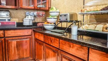 A breakfast buffet area with wooden cabinets, a coffee station, and a variety of food items displayed.