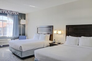 A hotel room with two beds, a bedside table with a lamp, a wall-mounted phone, and a window with curtains. - Quality Inn & Suites Roswell (Roswell)