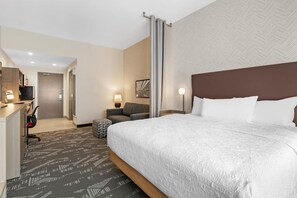 A hotel room with a large bed, a desk, a chair, a sofa, and a television. - Home2 Suites by Hilton Somerset (Somerset)