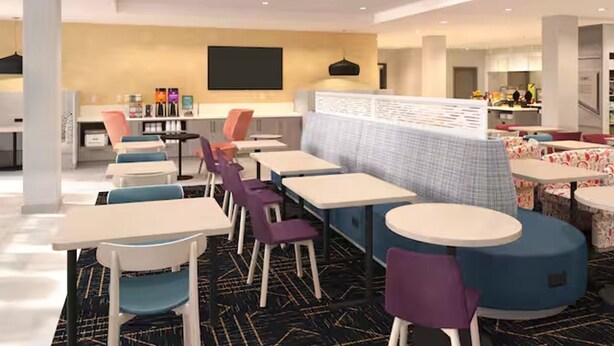 A modern dining area with tables and chairs, a kitchen in the background, and a partition wall. - Home2 Suites by Hilton Somerset (Somerset)