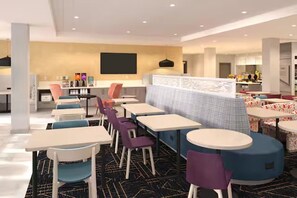 A modern dining area with tables and chairs, a kitchen in the background, and a partition wall. - Home2 Suites by Hilton Somerset (Somerset)