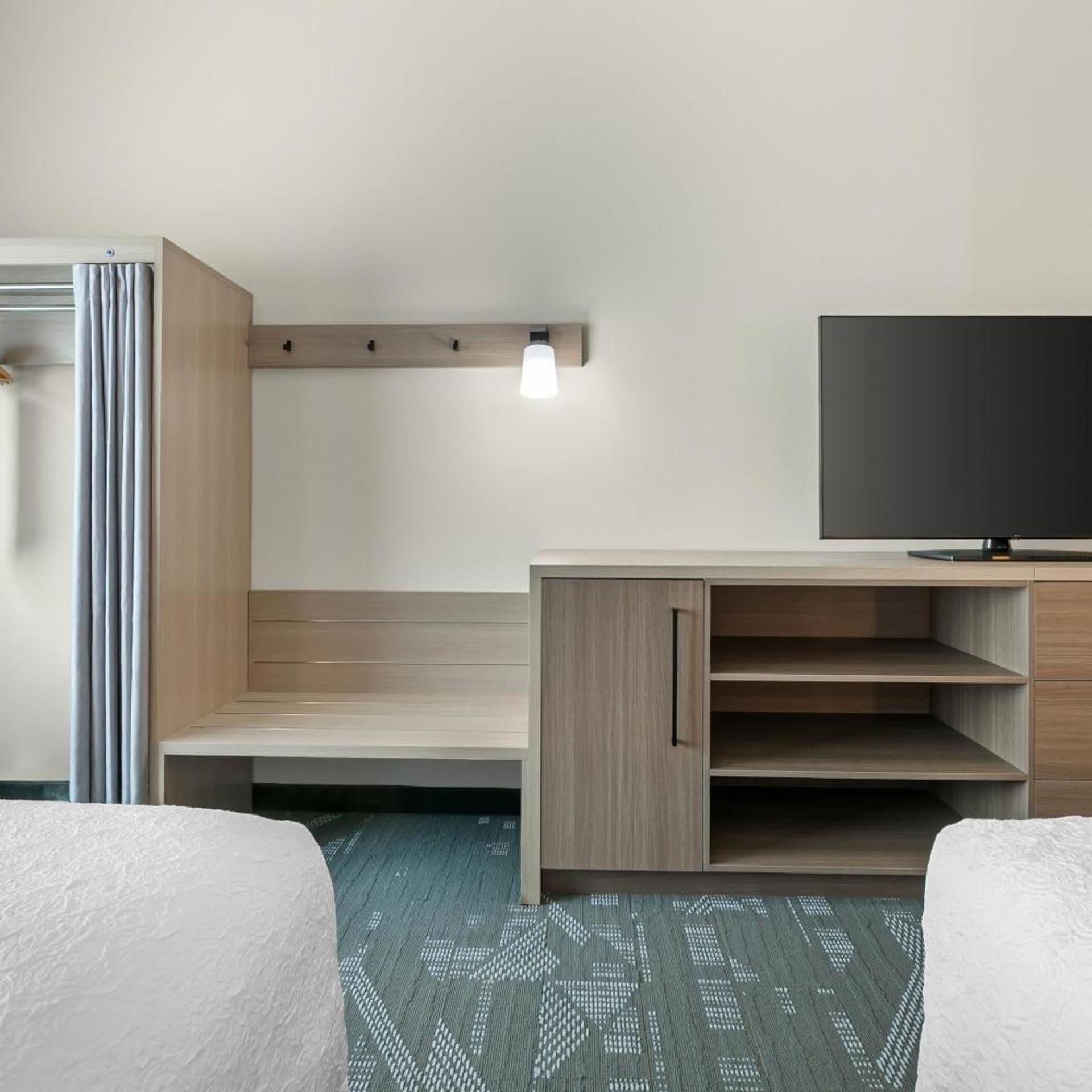 Quarto de hotel com uma cama, uma mesa, uma televisão e um candeeiro.