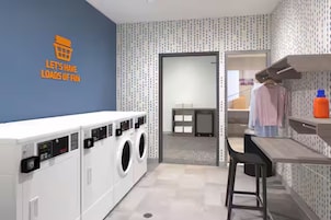 Un cuarto de lavado con pared azul, lavadora, secadora y una pequeña zona de bar con un taburete.