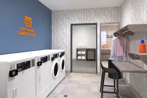 Un cuarto de lavado con pared azul, lavadora, secadora y una pequeña zona de bar con un taburete.