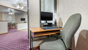 A hotel room with a desk, computer, and chair. There is a window with blinds, a ceiling fan, and a carpeted floor. - Econo Lodge Oacoma - Chamberlain West (Oacoma)
