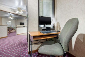Habitación de hotel con escritorio, computadora y silla. Tiene una ventana con persianas, ventilador de techo y piso alfombrado.