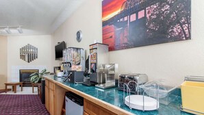A hotel room with a kitchenette, a flat-screen TV, a painting of a sunset, and a green carpet. - Econo Lodge Oacoma - Chamberlain West (Oacoma)