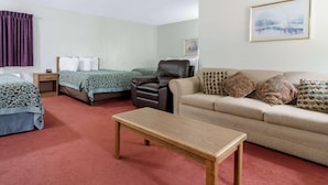 A hotel room with two beds, a sofa, a leather chair, a wooden table, and a painting on the wall. - Econo Lodge Oacoma - Chamberlain West (Oacoma)