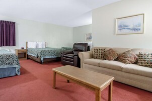Habitación de hotel con dos camas, un sofá, un sillón de cuero, una mesa de madera y un cuadro en la pared.