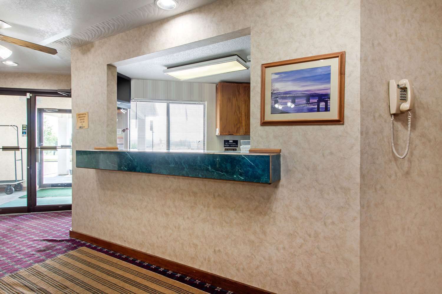 A reception area with a marble counter, a framed picture, a telephone, and a door leading outside.
