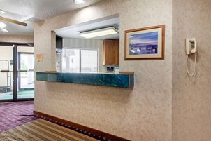 Zona de recepción con mostrador de mármol, un cuadro enmarco, un teléfono y una puerta que da al exterior.