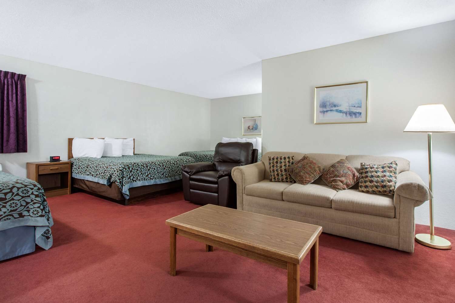 A hotel room with two beds, a sofa, a coffee table, and a lamp.