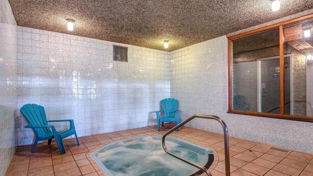 A spa area with a hot tub, two blue chairs, and a window. - Vernon Motel (Vernon)