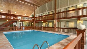 A large indoor swimming pool with a wooden deck surrounding it, multiple balconies, and a staircase leading to an upper level. - Vernon Motel (Vernon)