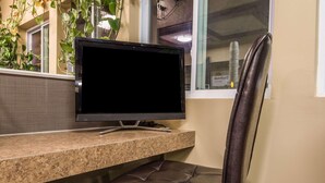 A workspace with a computer monitor on a granite countertop, a leather chair, and a window with blinds. - Vernon Motel (Vernon)