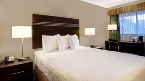 A hotel room with a large bed, two bedside lamps, a desk with a chair, and a window with curtains. - Vernon Motel (Vernon)