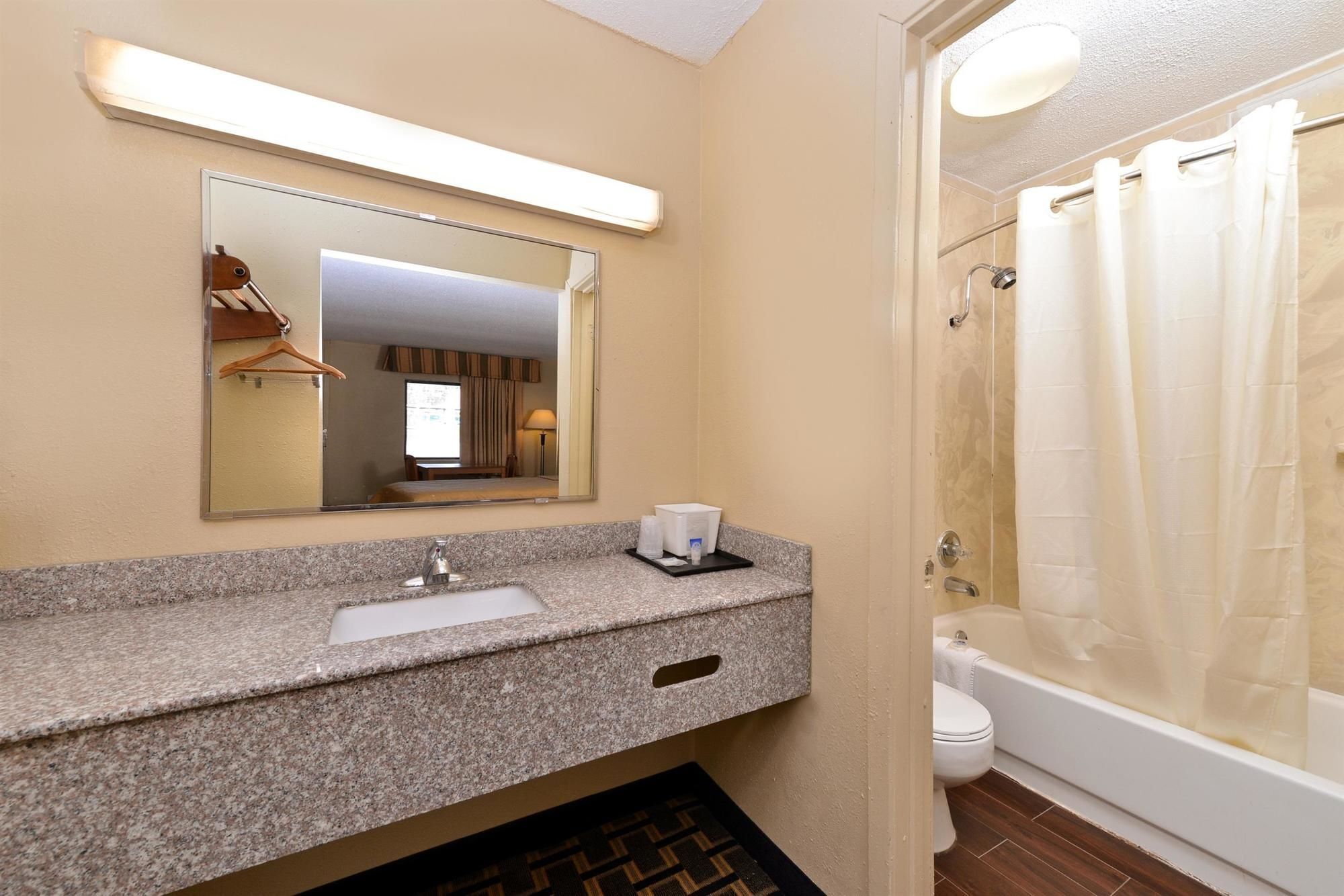 Une salle de bain avec un comptoir en granit, un lavabo, un miroir, une douche avec un rideau et des toilettes.