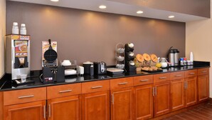 Uma cozinha de hotel com um espaço para café, uma máquina de waffles e diversos eletrodomésticos.