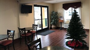 A dining area with tables and chairs, a potted plant, a Christmas tree, and a television on the wall. - Red Roof Inn Kimball, TN - I-24 (South Pittsburg)