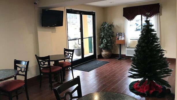 A dining area with tables and chairs, a potted plant, a Christmas tree, and a television on the wall. - Red Roof Inn Kimball, TN - I-24 (South Pittsburg)