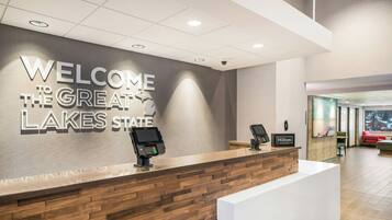 Un mostrador de recepción con un cartel que dice 'Welcome to the Great Lakes State', un quiosco digital y una placa de 'Hilton Honors'.