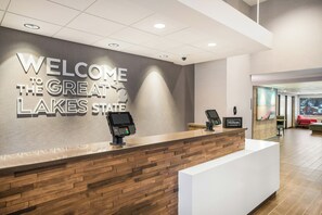 A reception desk with a 'Welcome to the Great Lakes State' sign, a digital kiosk, and a 'Hilton Honors' plaque. - Hampton Inn & Suites Houghton (Houghton)