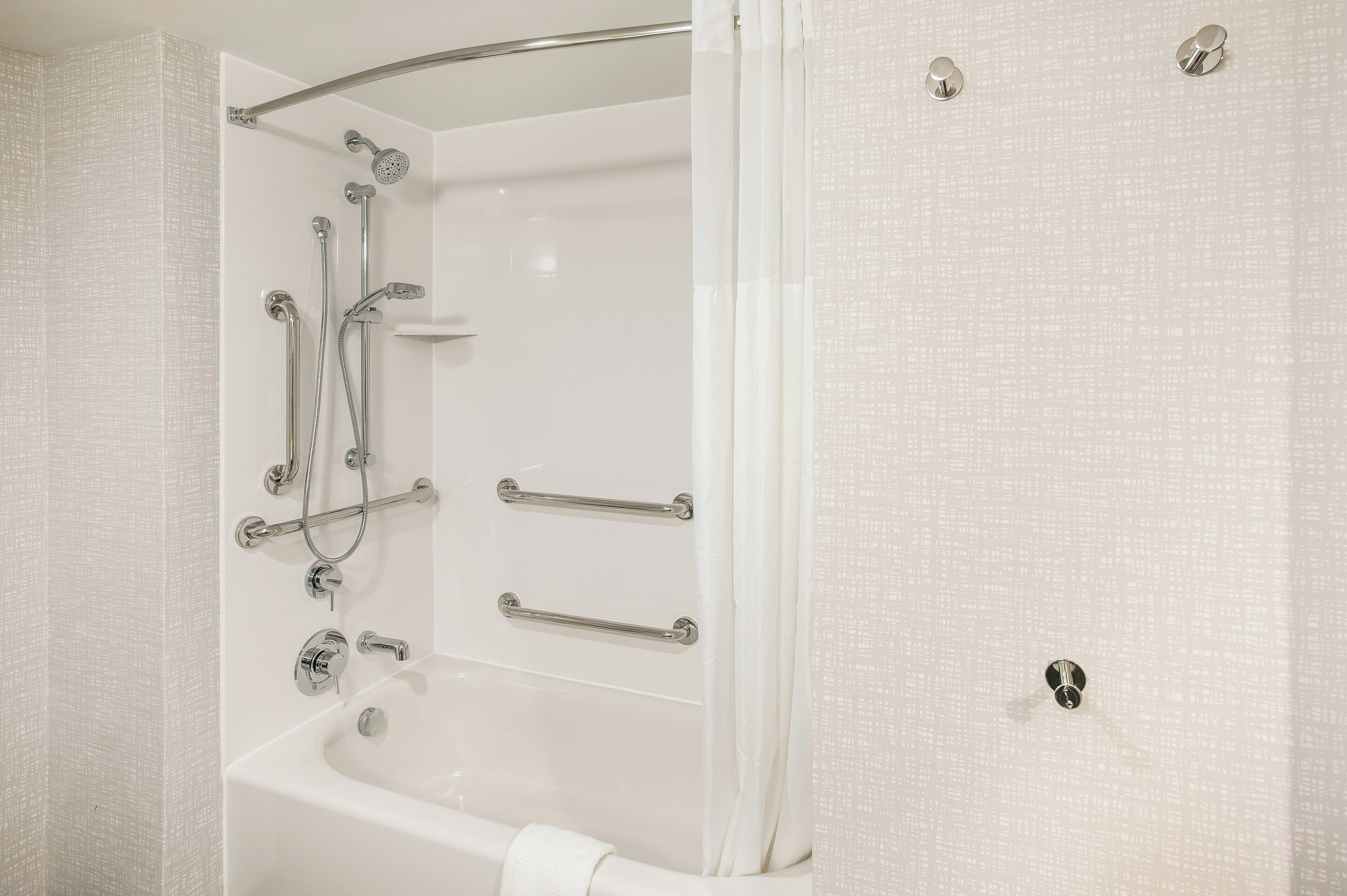 A modern bathroom with a bathtub, shower, and handrails.