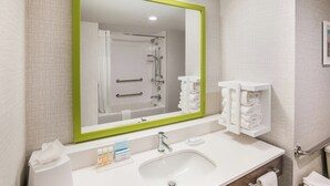 Un baño con un espejo grande, un lavamanos, un perchero para toallas y una ducha.