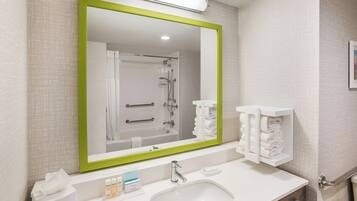 A bathroom with a large mirror, a sink, a towel rack, and a shower.