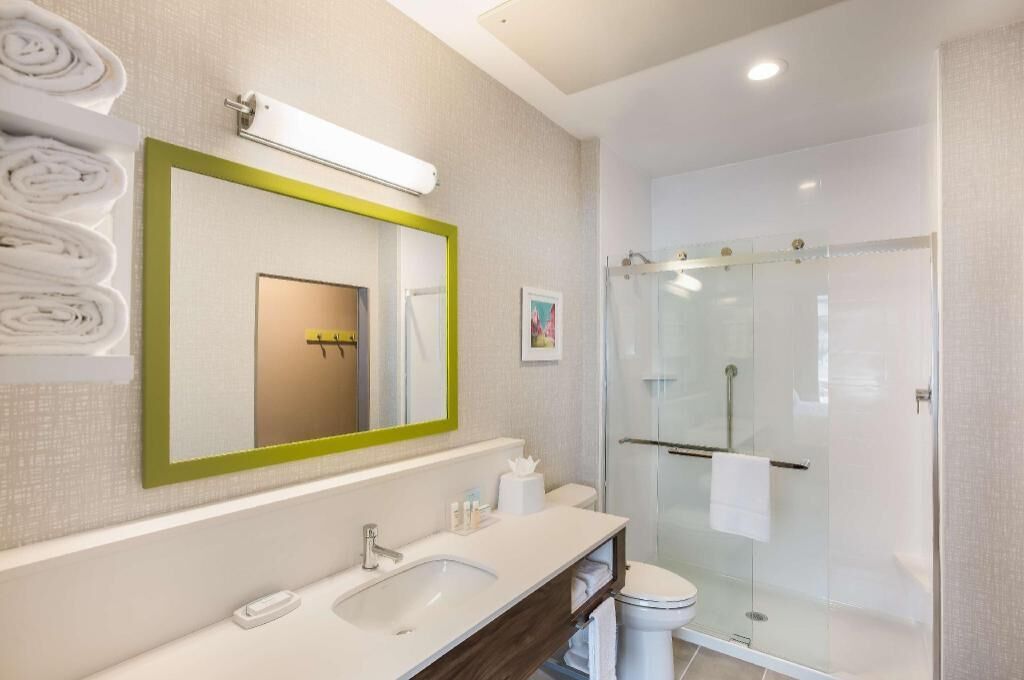 A modern bathroom with a large mirror, a sink, a toilet, and a glass-enclosed shower.