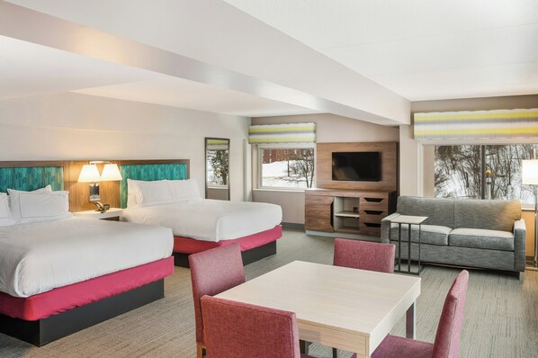 Habitación de hotel con dos camas, un sofá, un televisor y una zona de comedor.