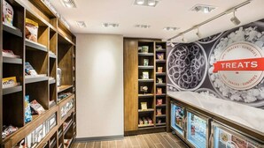 Una sección bien iluminada de aperitivos y artículos varios, con estantes llenos de diferentes bocadillos y un expositor refrigerado.