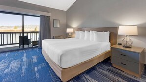 A hotel room with a large bed, two bedside tables with lamps, a chair, and a view of the outdoors.