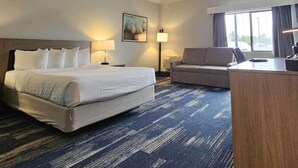 A hotel room with a large bed, a sofa, a desk, and a window.