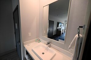 A modern bathroom with a white sink, a large mirror, and a towel rack. - Edgewater Inn and Suites, Ascend Hotel Collection (Coos Bay)
