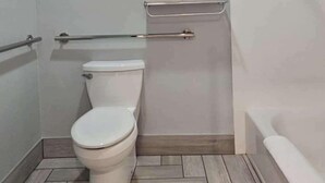 A bathroom with a toilet, a grab bar, a towel rack, and a bathtub.