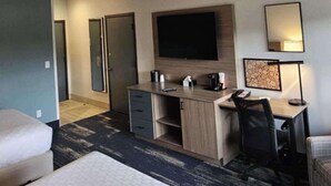 A hotel room with a bed, a desk, a chair, a TV, and a mirror.