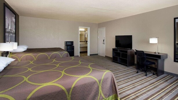 Une chambre d’hôtel avec un grand lit, un bureau avec une chaise, une télévision et une porte donnant sur une salle de bain.
