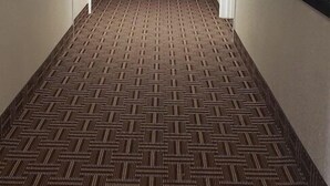 Un couloir avec un tapis à motifs, des murs blancs et des portes de part et d’autre.
