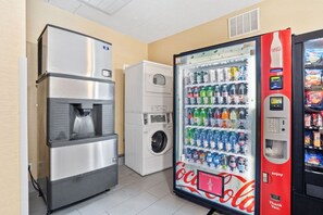 A vending machine with a Coca-Cola logo, a water dispenser, and a washing machine. - Blue Water Inn & Suites, Bw Signature Collection (Sneads Ferry)