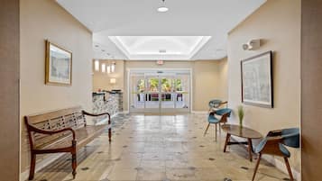 A hotel lobby with a wooden bench, a reception desk, and a glass door entrance.
