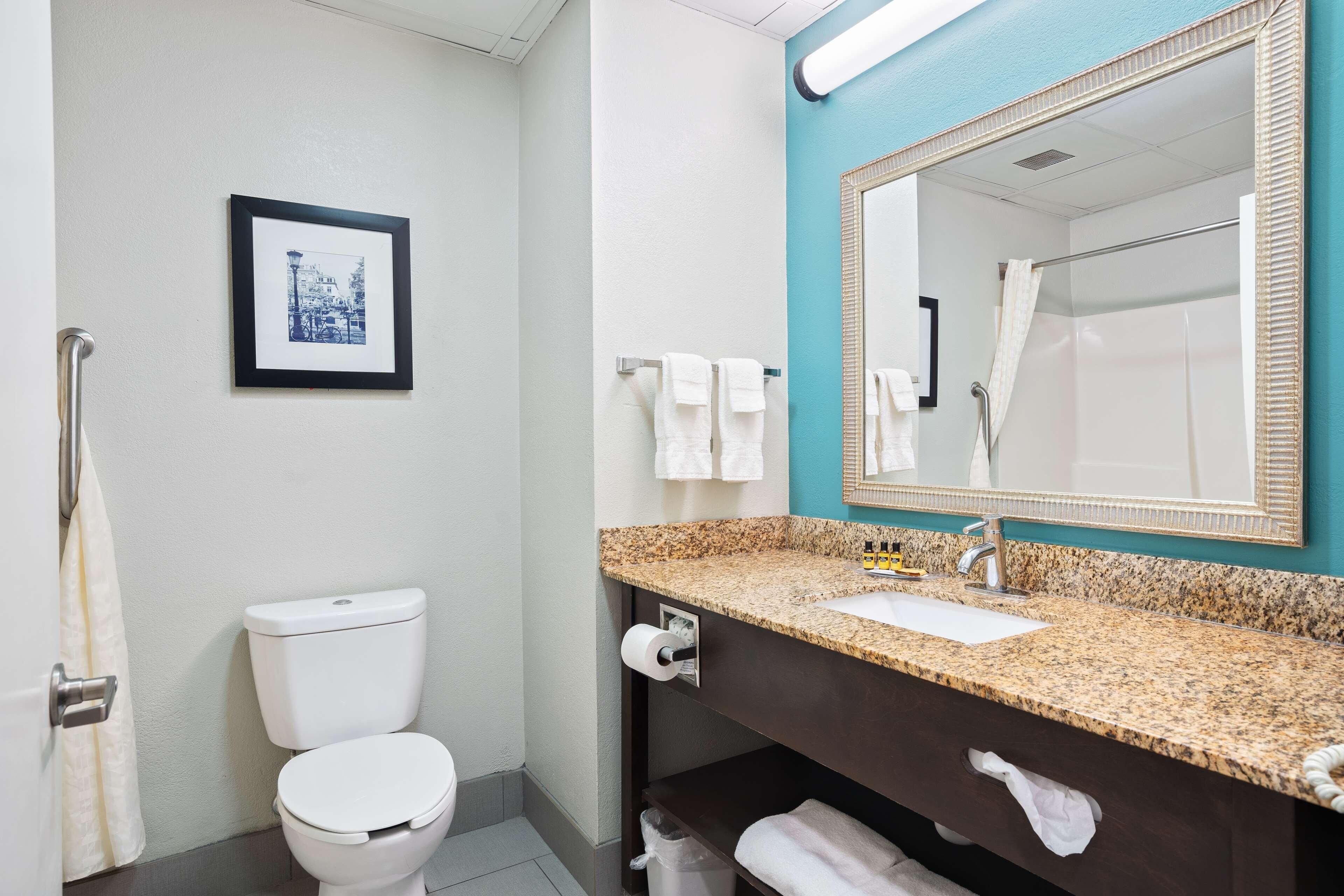 A bathroom with a toilet, sink, mirror, and towel rack.