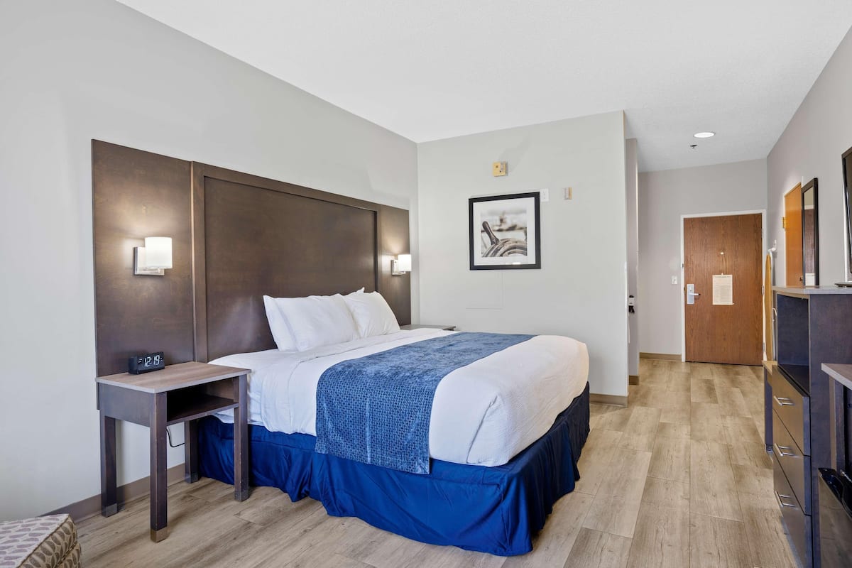 A hotel room with a bed, bedside table, wall-mounted light, and a framed picture.