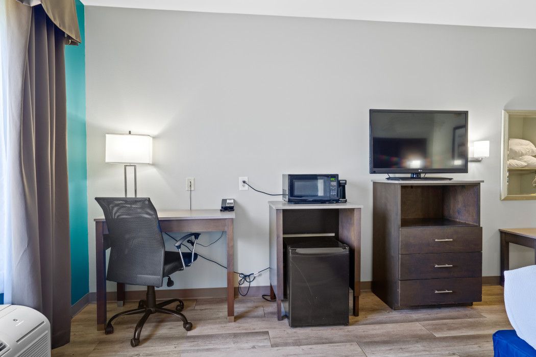 Habitación de hotel con escritorio, silla, microondas, televisor y un refrigerador pequeño.