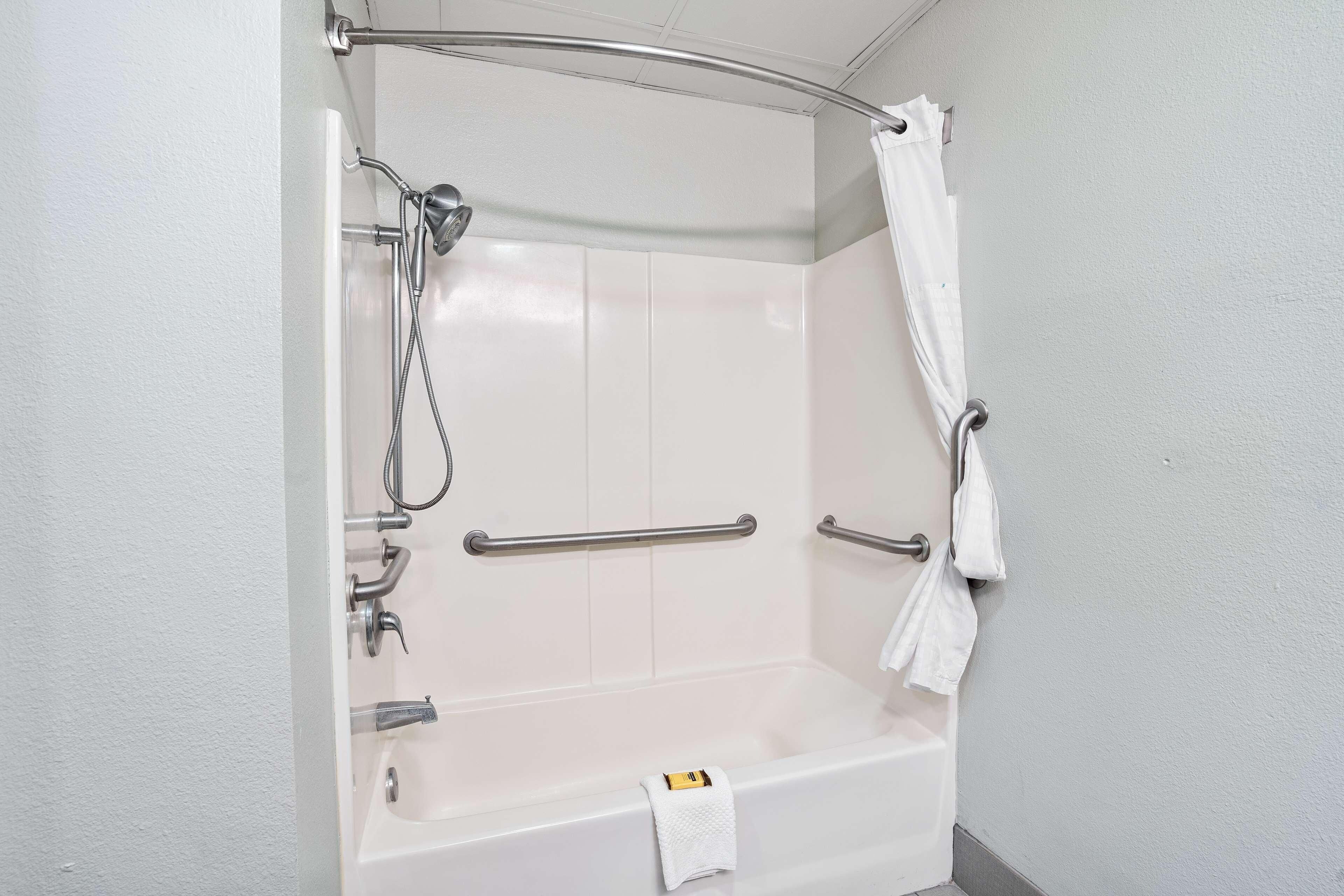 Ein Badezimmer mit einer weißen Badewanne, Haltegriffen, einer Duschbrause und einem Handtuchhalter.