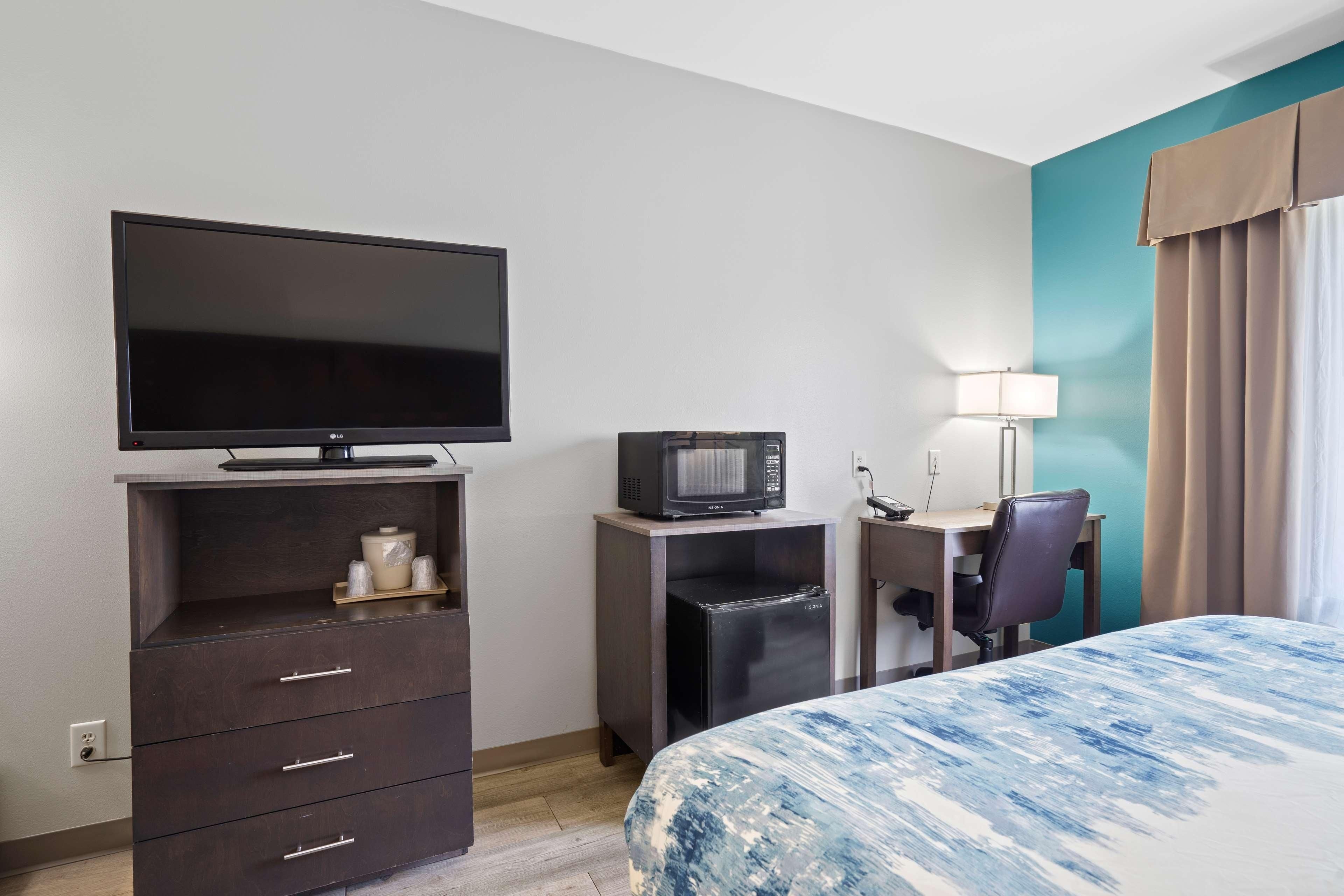 Quarto de hotel com cama, televisão, micro-ondas, frigorífico, secretária e cadeira.
