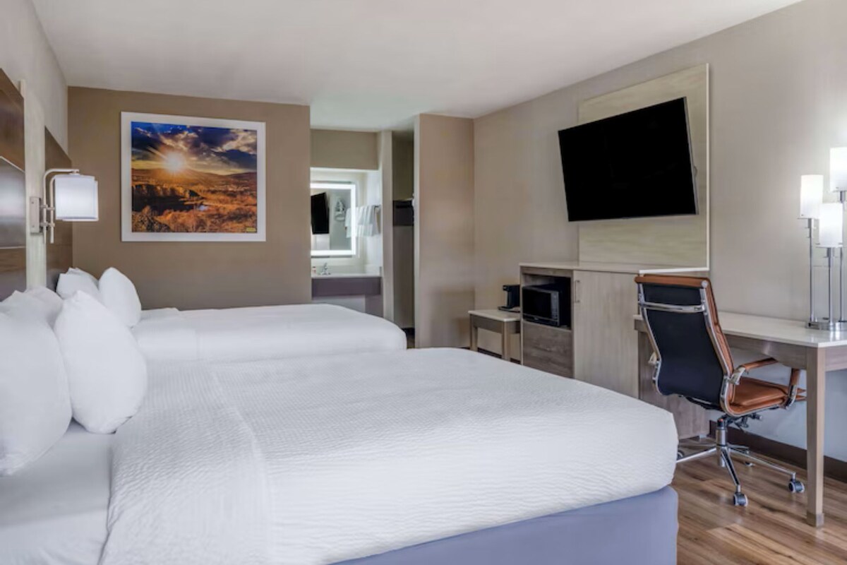 A hotel room with a large bed, a desk with a chair, a flat-screen TV, and a painting on the wall.
