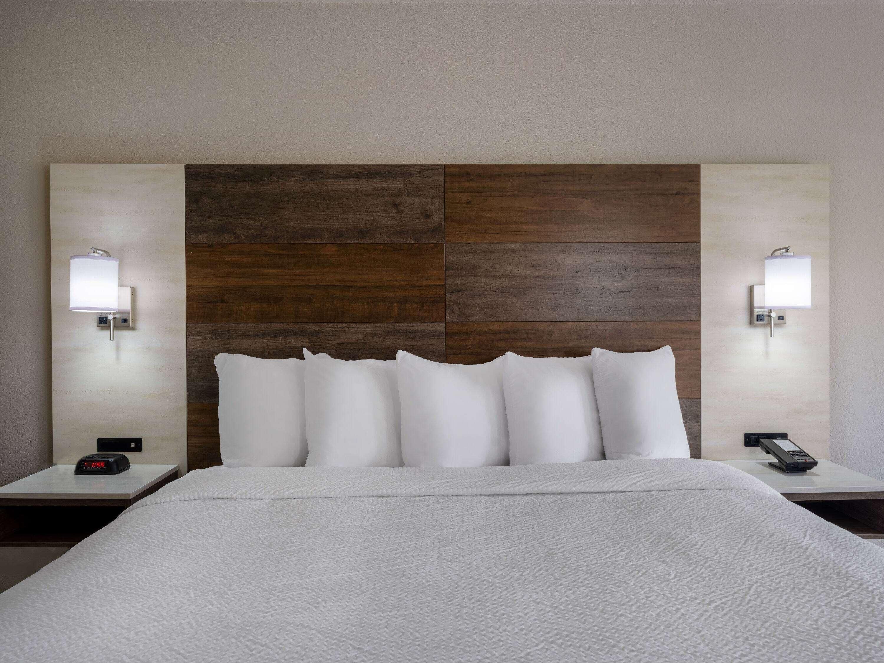 A hotel room with a large bed, two bedside tables, a clock, a remote control, and wall-mounted lamps.