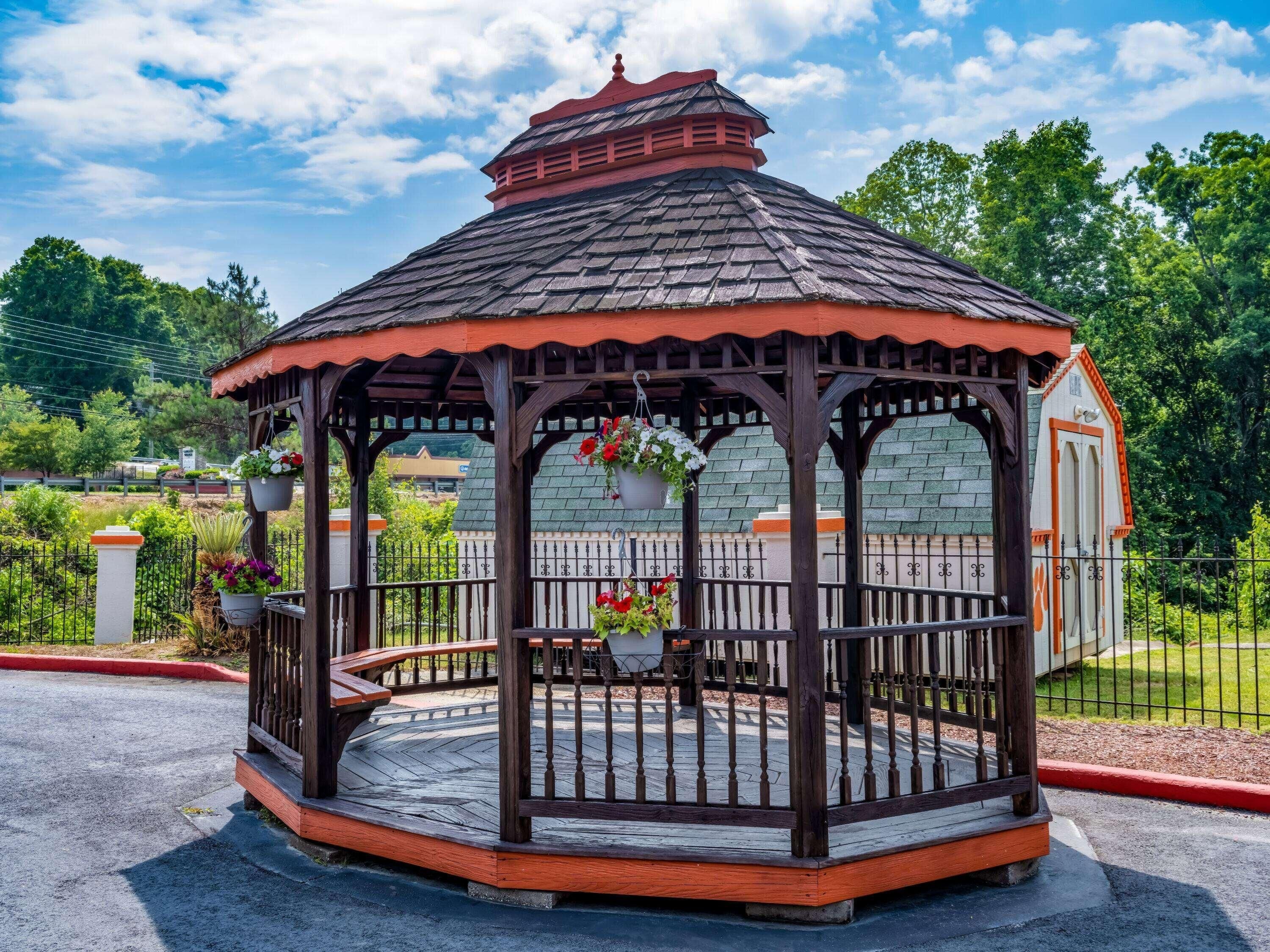 A gazebo with a tiled roof, wooden pillars, and a fenced area with hanging flower baskets.